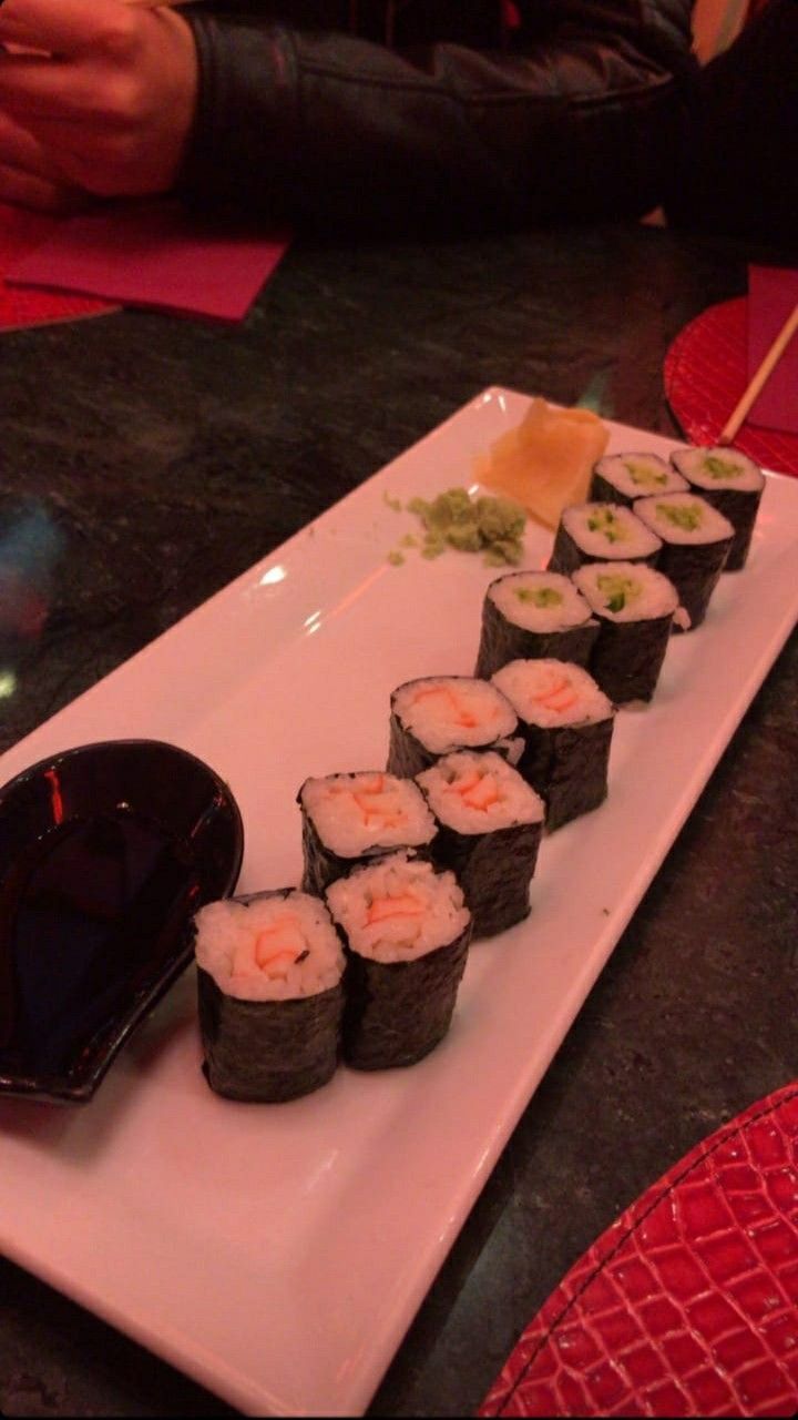 sushi is served on a white plate with chopsticks in the foreground