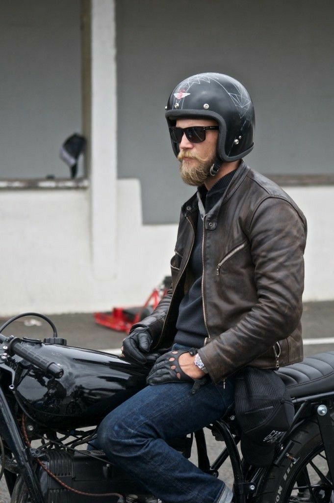 a man sitting on top of a motorcycle wearing a leather jacket and black helmet with his hands in his pockets