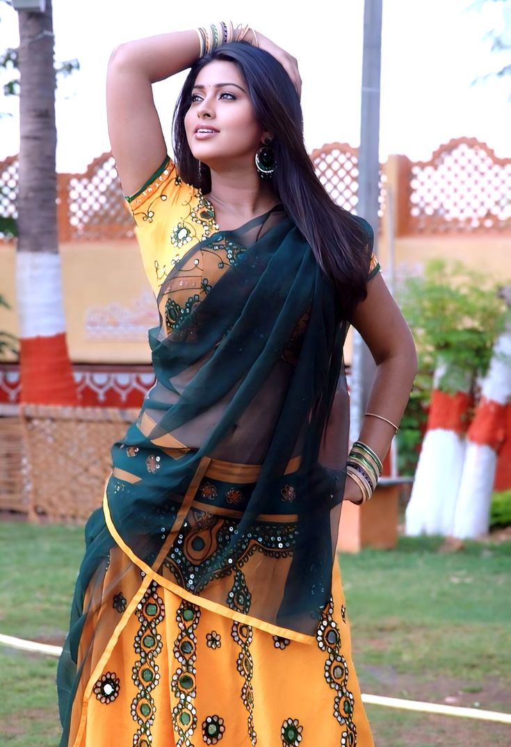 a woman in a yellow and green sari dancing with her hands behind her head