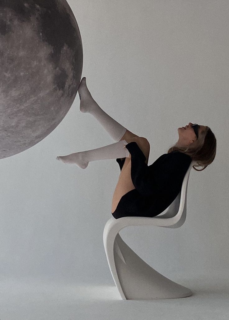 a woman sitting on a chair with her legs up in the air next to a large moon