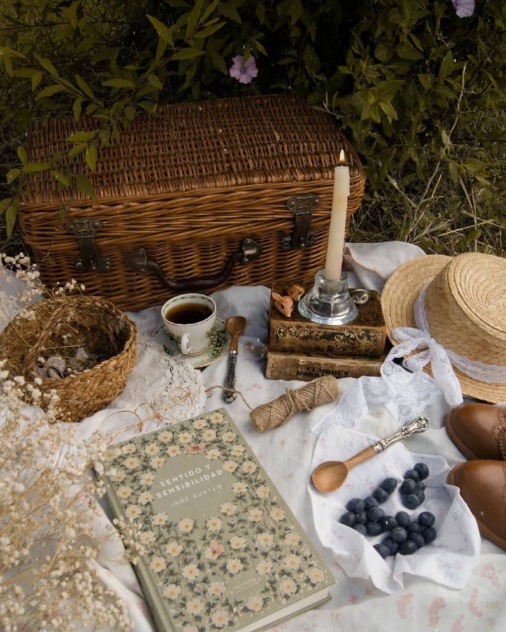 an old fashioned picnic set up on a blanket with books, candles and other items