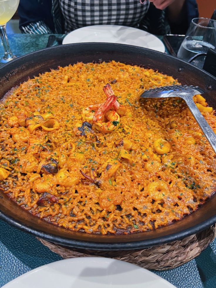 a large pan filled with food sitting on top of a table next to wine glasses