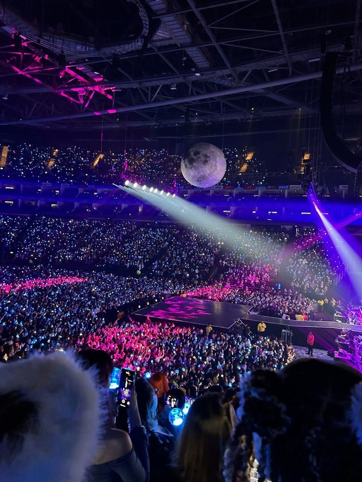 a large crowd at a concert with bright lights on the stage and people in the audience