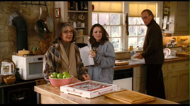 three people standing in a kitchen with an apple bowl on the counter and one holding a piece of paper