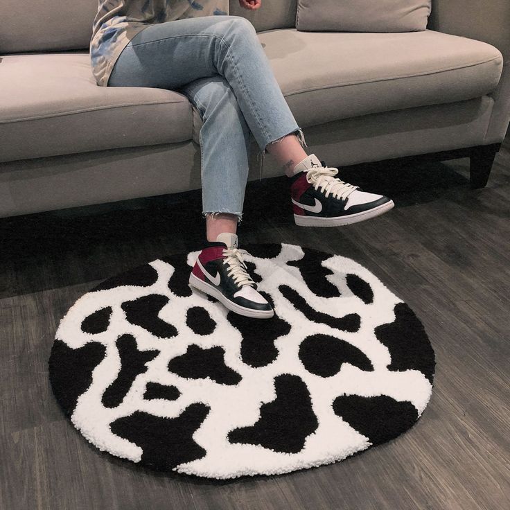 a woman sitting on top of a black and white animal print rug in front of a couch