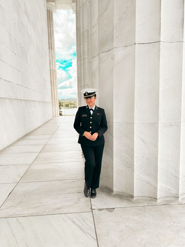 a woman in uniform standing next to a wall with columns on both sides and the sky behind her