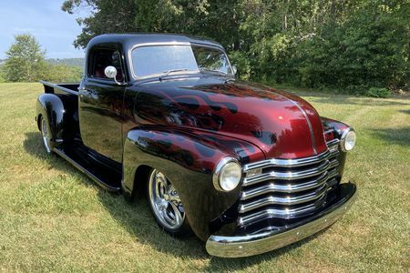 an old red and black truck parked in the grass