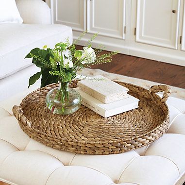 a wicker tray with flowers and books on it sitting on a white ottoman in a living room