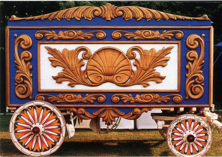 an elaborately painted wooden cart with wheels on the grass in front of some trees