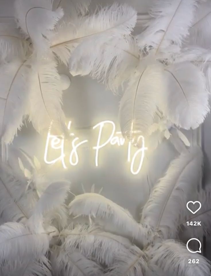 the words let's party are lit up in front of white feathers and hearts