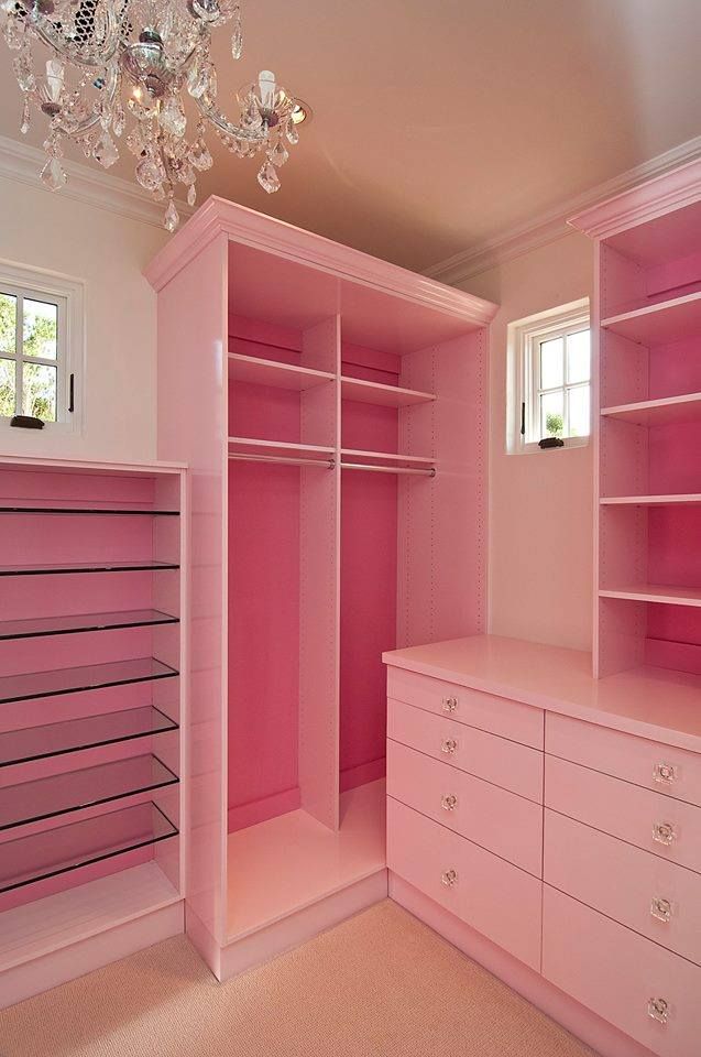 a pink closet with chandelier hanging from the ceiling and drawers in front of it