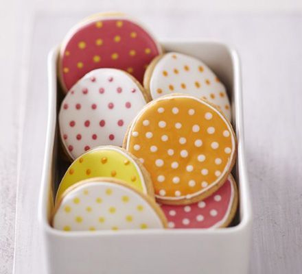 some decorated cookies in a white box on a wooden table with polka dotty fabric