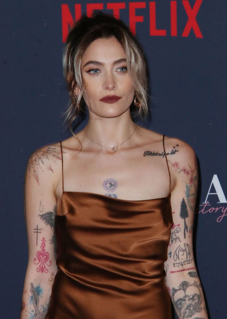 a woman with tattoos standing in front of a netflix sign and posing for the camera