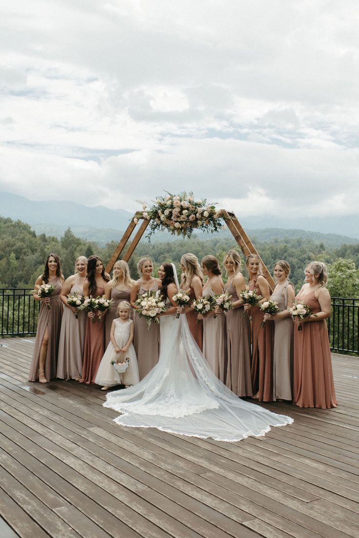 a group of women standing next to each other in front of a wedding arch on top of a wooden deck