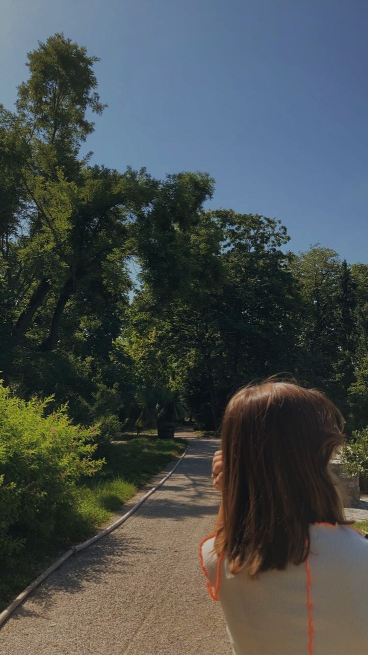 a woman standing on the side of a road looking up at a kite flying in the air