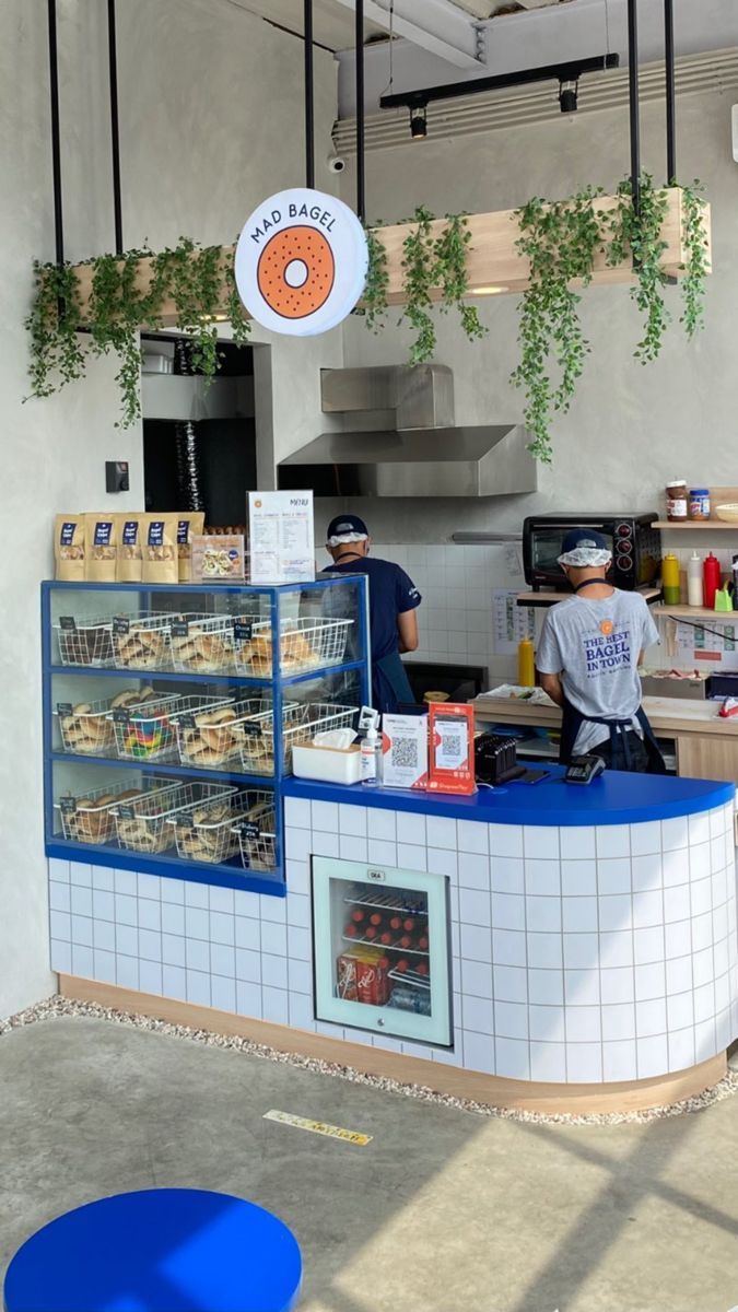 the inside of a doughnut shop with people working behind the counter and hanging plants on the ceiling