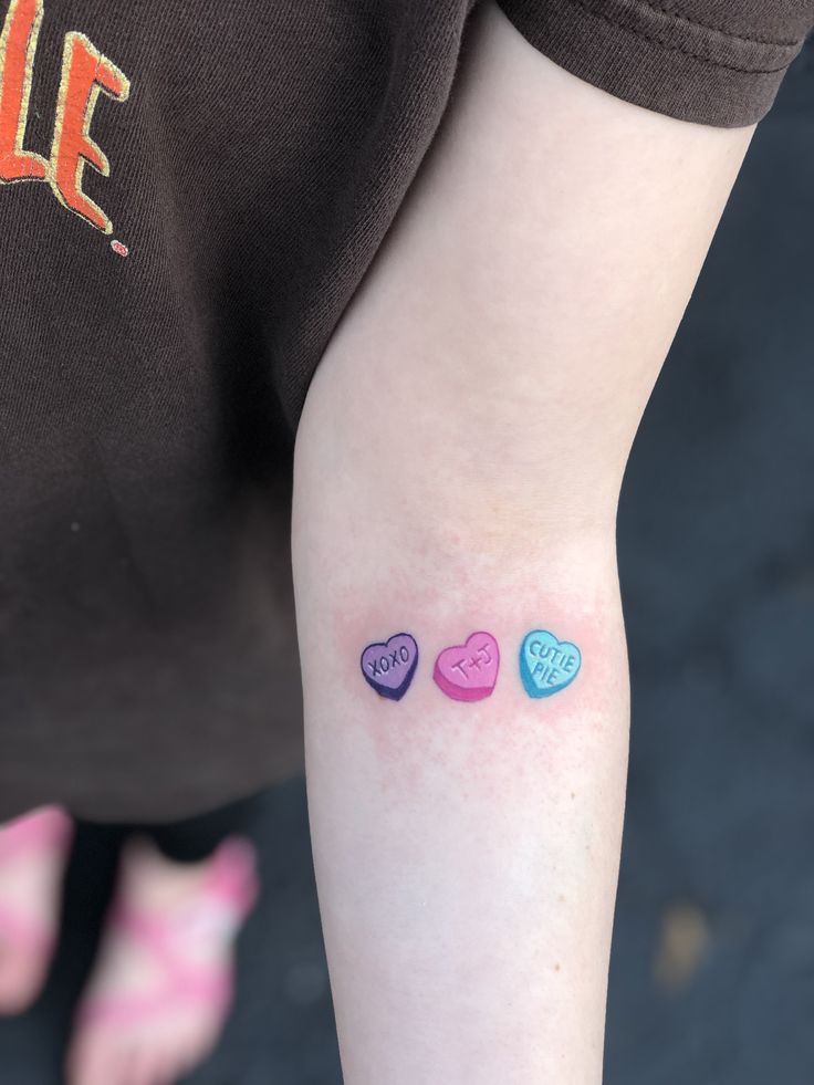 three small hearts on the left arm, one is blue and one is pink with an orange heart