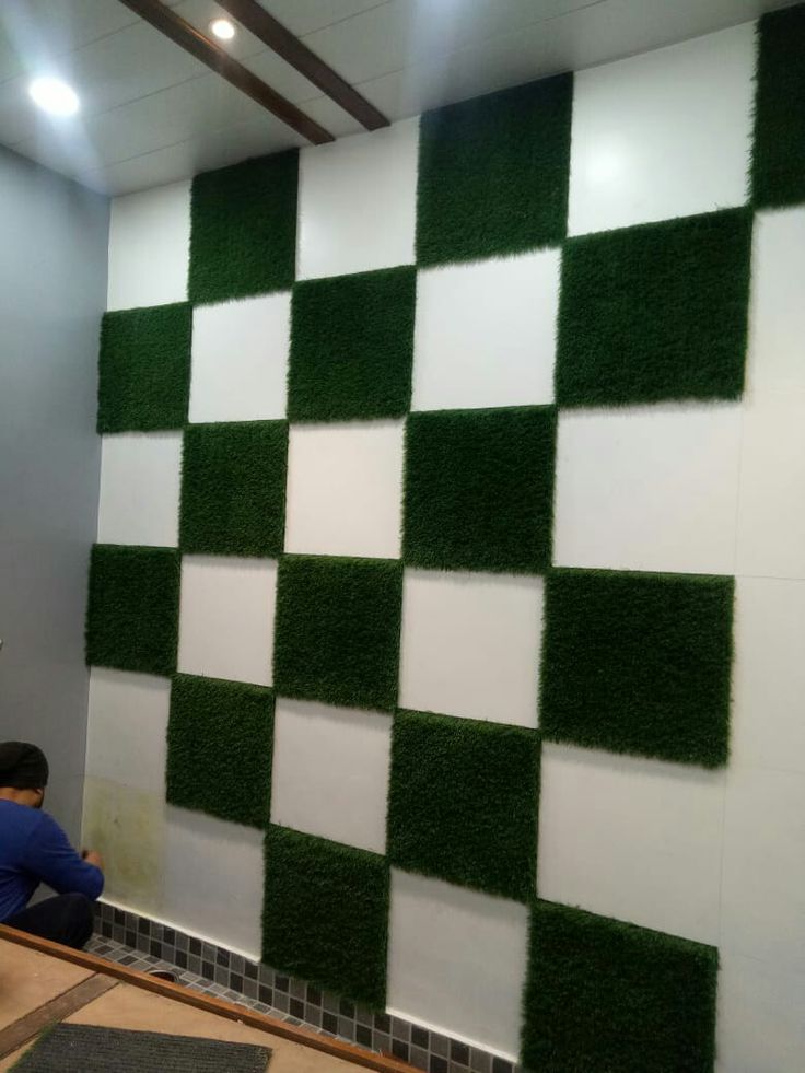 a man sitting in front of a wall covered in fake grass