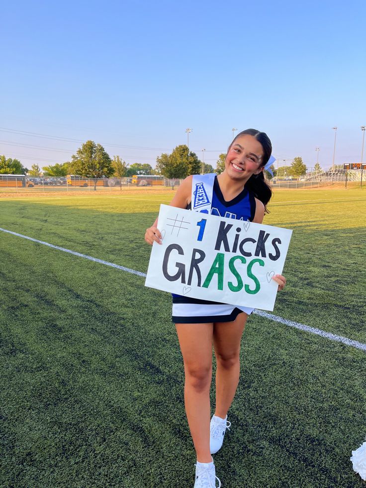 a girl holding a sign that says 1 kicks grass on it in front of a soccer field