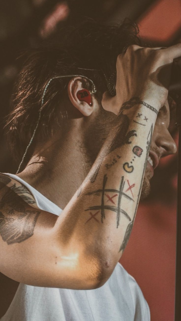 a man with tattoos on his arm and shoulder holding a microphone in front of him