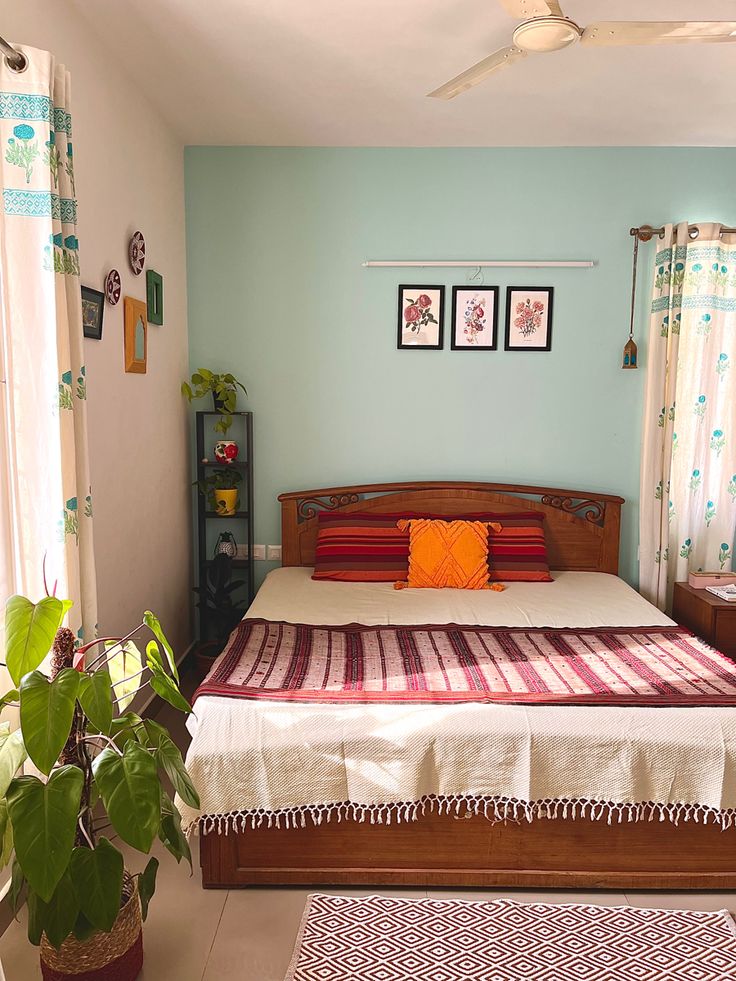 a bed room with a neatly made bed and a plant in the corner on the floor