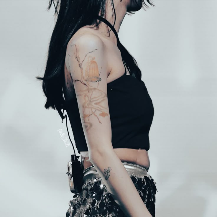 a woman with long black hair and tattoos on her arm, holding a handbag