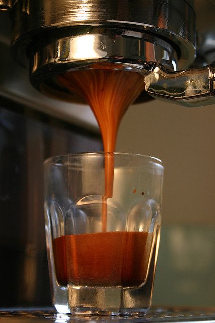 an espresso machine pouring coffee into a glass on top of a wooden table