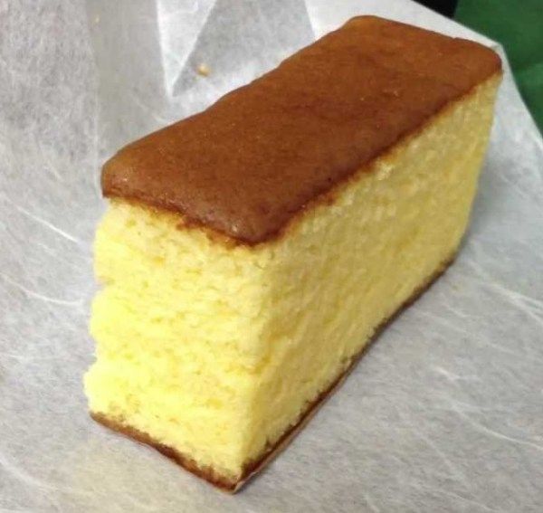 a piece of yellow cake sitting on top of a white paper wrapper covered in wax paper