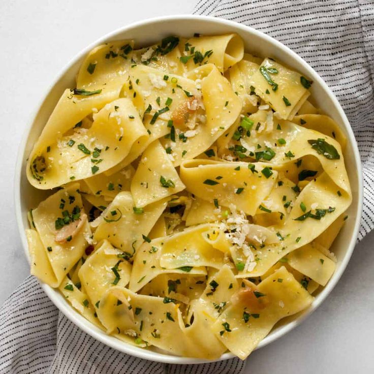 a white bowl filled with pasta covered in parmesan cheese and garnished with herbs