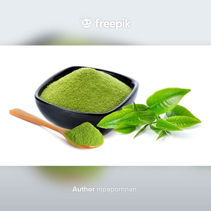 green powder in a black bowl next to a wooden spoon with leaves on the side