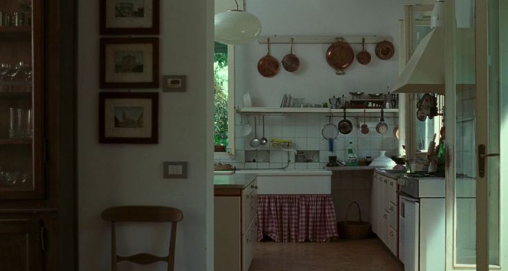 an open kitchen with pots and pans hanging from the ceiling, next to a dining room table