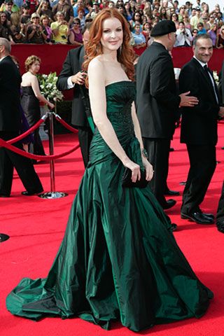 a woman in a green dress standing on a red carpet with people behind her looking at the camera