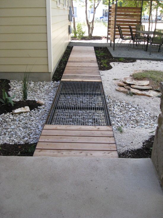 a walkway made out of wood and metal in front of a house with gravel on the ground