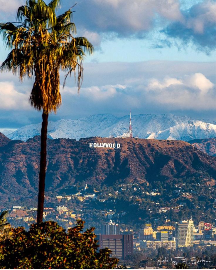 the city is surrounded by mountains and palm trees in front of it, with snow capped mountains in the background