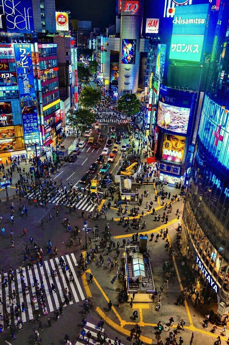 an aerial view of a city at night with many people crossing the street and buildings lit up