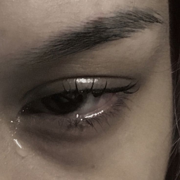 a woman's eye with water drops on the iris and her black hair is in the background