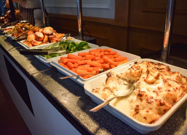 several trays of food are lined up on a buffet table with utensils