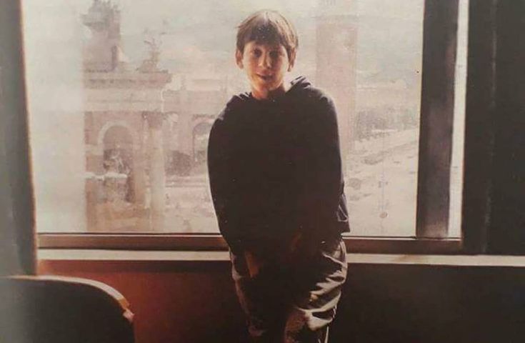 a young boy standing in front of a window