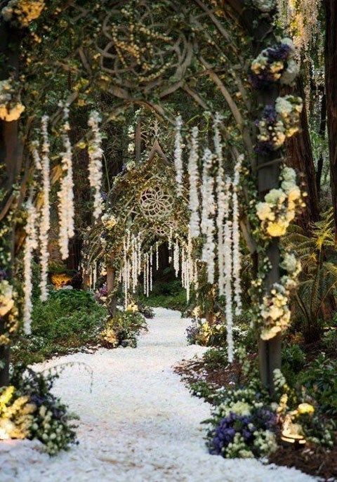 an outdoor garden with lots of flowers and greenery on the walkway, surrounded by trees