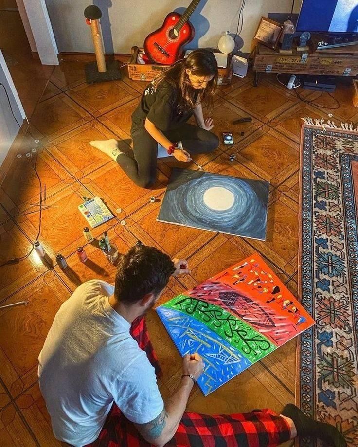 two people are sitting on the floor with their paintings and guitar in front of them