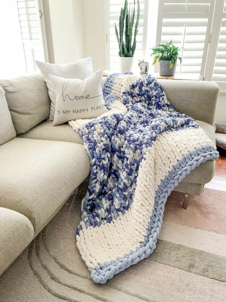 a blue and white crocheted blanket sitting on top of a couch next to a pillow