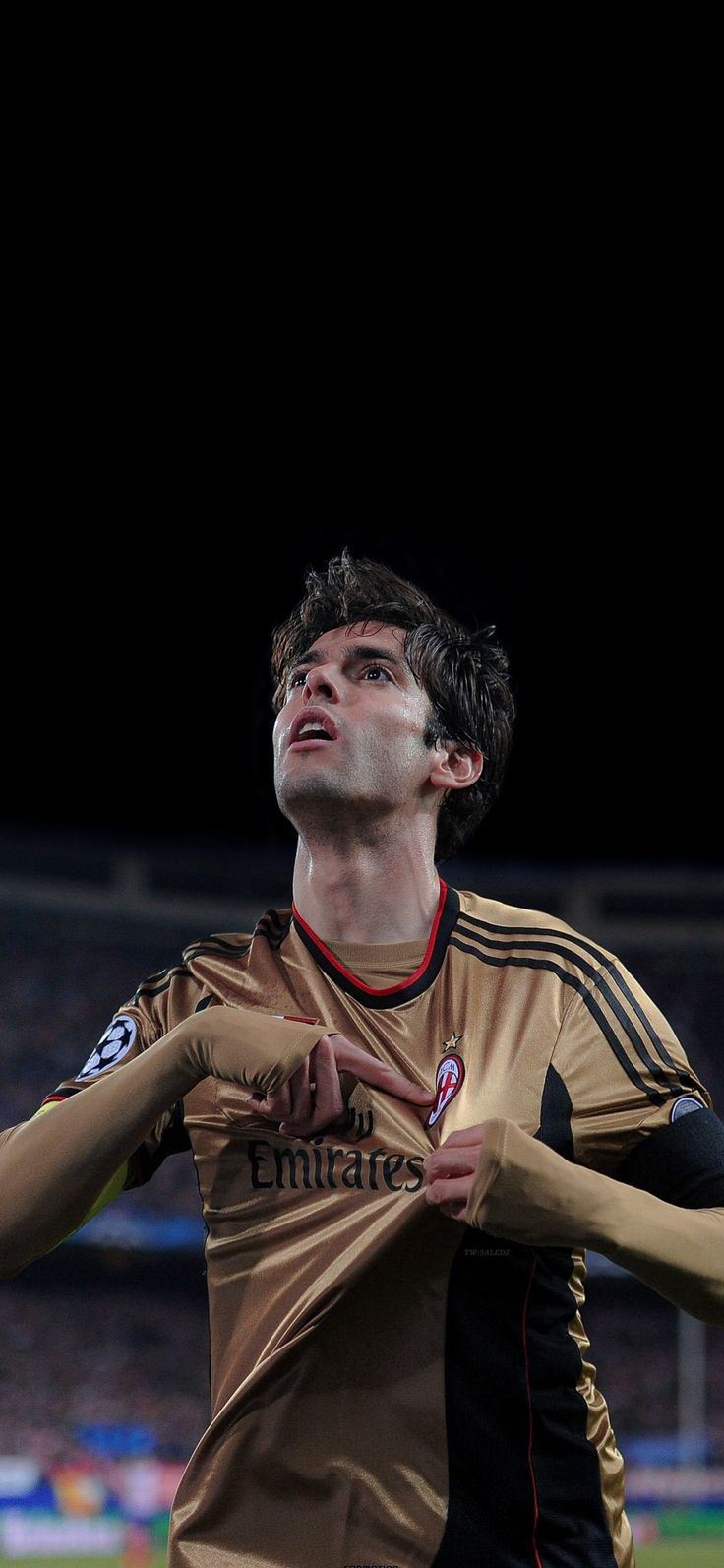 a young man holding a soccer ball on top of a lush green field in front of an empty stadium