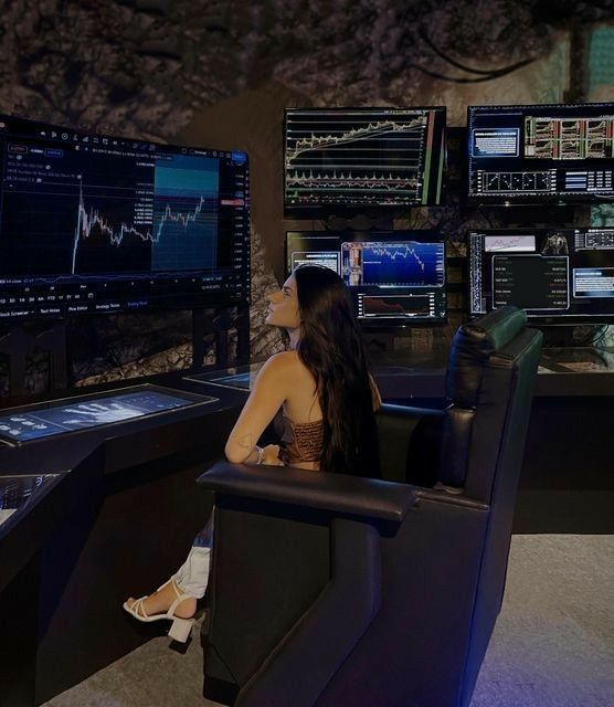 a woman sitting at a desk in front of multiple monitors