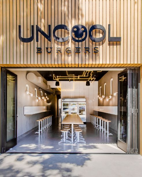 the entrance to an outdoor cafe with tables and stools in front of it that says uncool