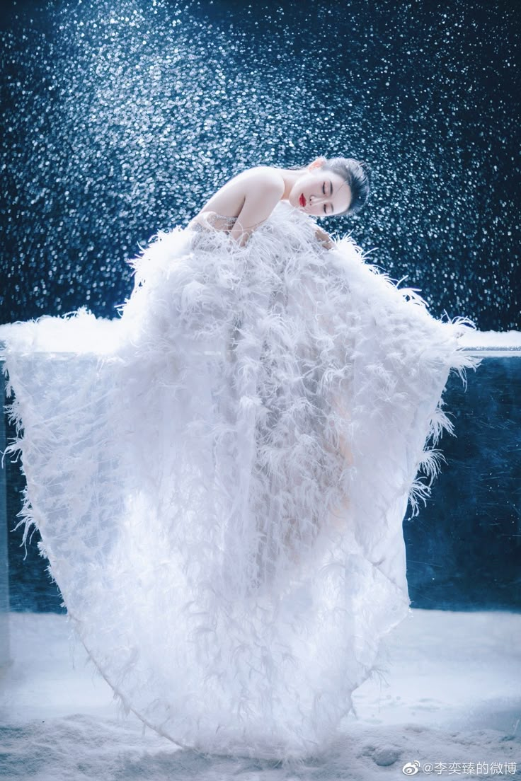 a woman in a white dress with feathers on her back, standing under water droplets