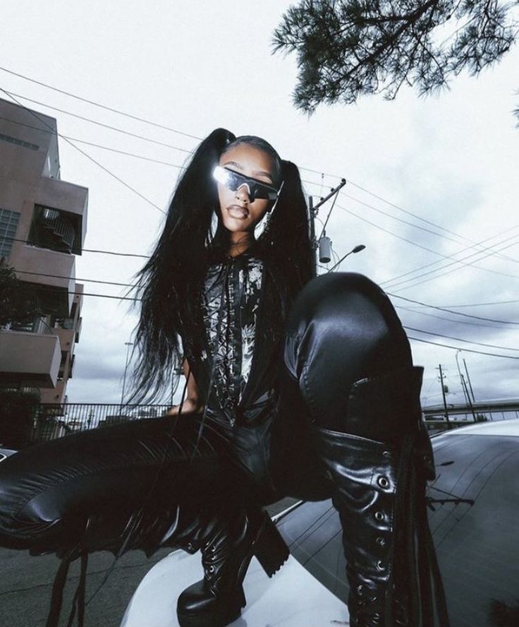 a woman sitting on top of a car wearing black leather pants and knee high boots