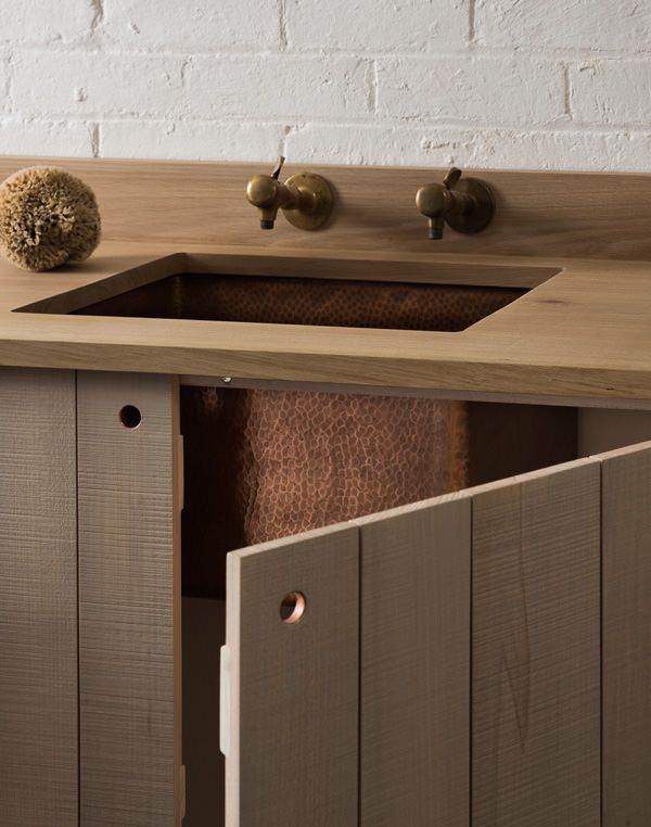 a wooden sink with two faucets on the side and a brick wall behind it