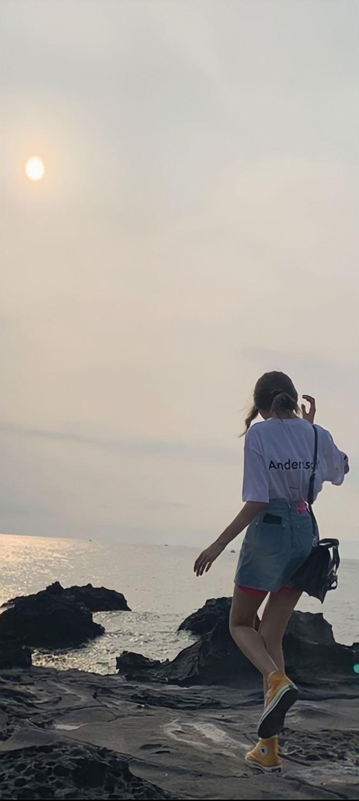 a woman standing on top of a rocky beach next to the ocean