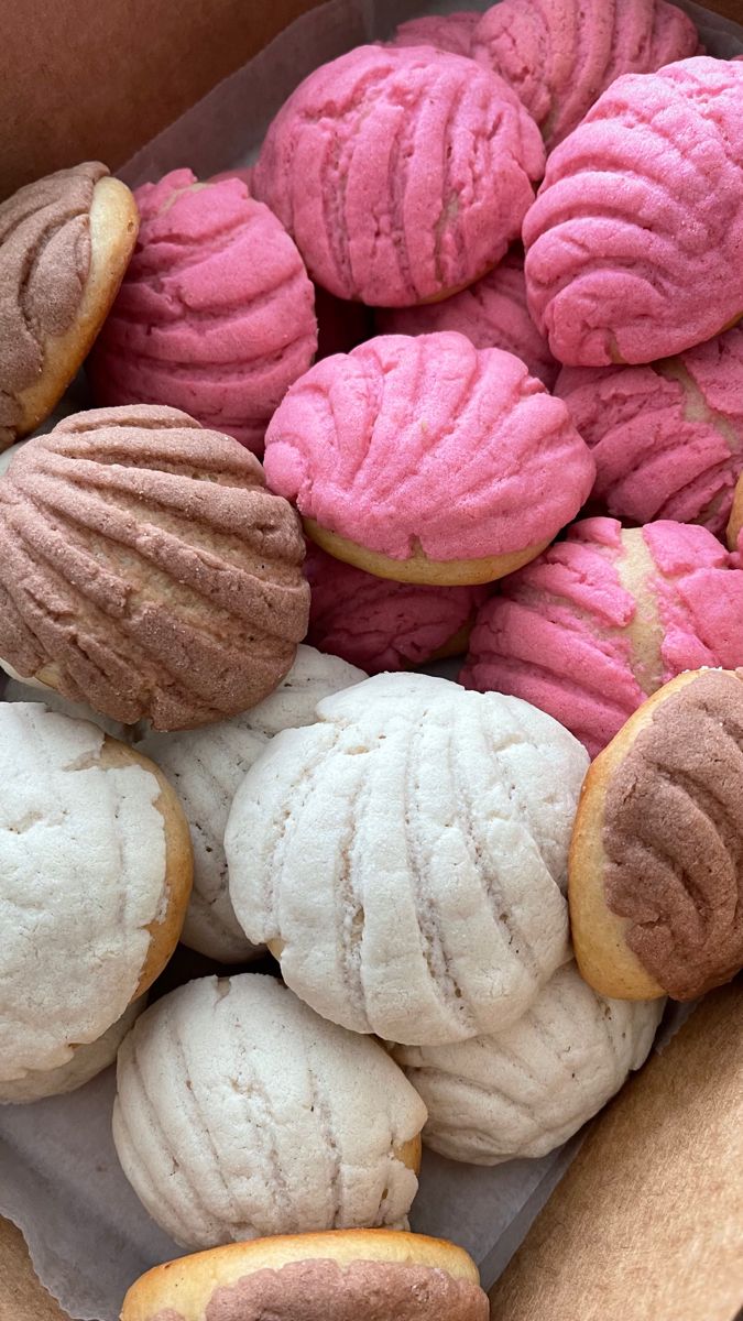 a box filled with pink and white frosted pastries on top of a table