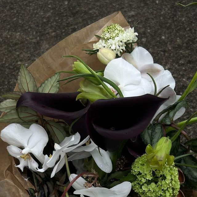 a bouquet of flowers sitting on top of a brown paper bag with white and green flowers